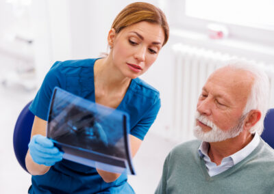 Zahnärztin erklärt einem älteren Patienten Behandlungsschritte